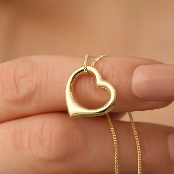 Gold heart-shaped necklace held between fingers against a neutral background