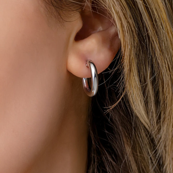 Close-up of an ear wearing a silver hoop earring with blurred hair and skin in the background