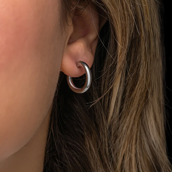 Close-up of a person wearing a silver hoop earring with brown hair.