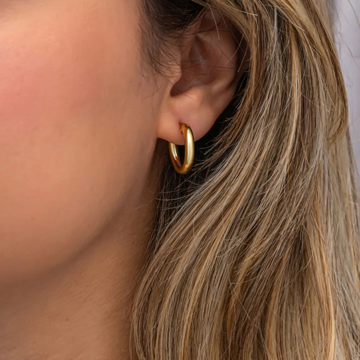 Close-up of a person wearing a gold hoop earring with blonde hair.