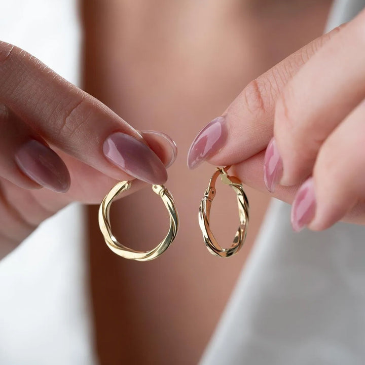 Gold hoop earrings held between two fingers with a blurred background