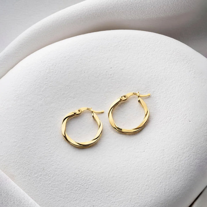 Gold hoop earrings on a white cushion
