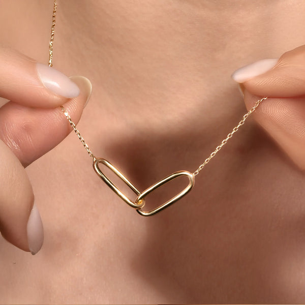 Gold necklace with a unique link design held by a hand against a neutral background