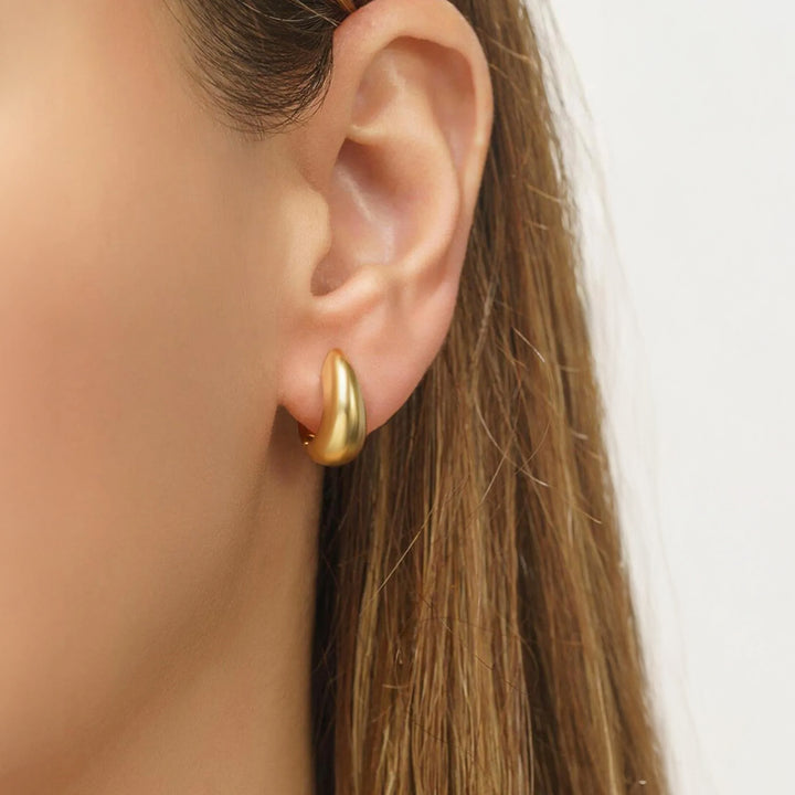 Gold hoop earring worn by a person with long hair on a neutral background