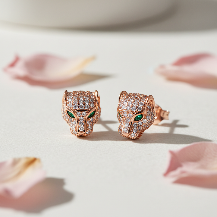 Rose gold panther head earrings with green eyes on a light background with pink petals.
