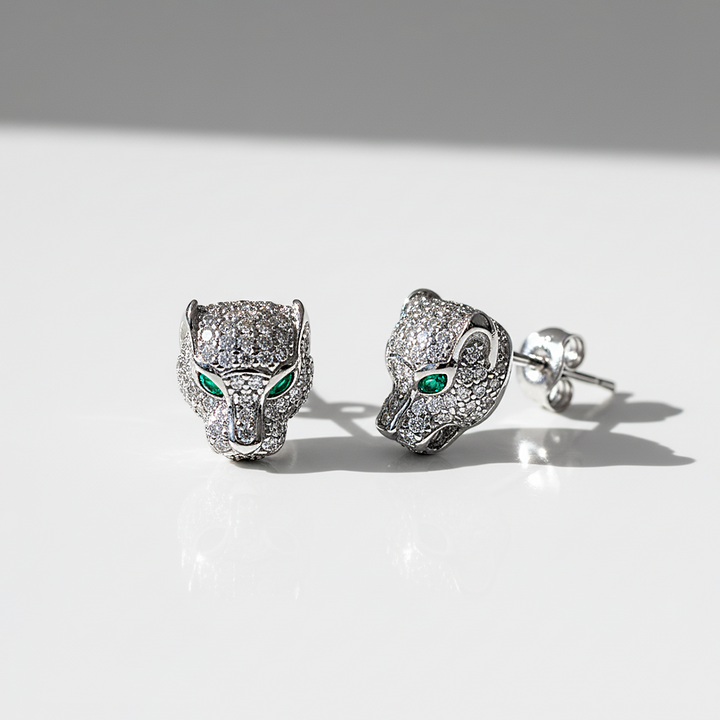 Silver panther head earrings with green gemstones on a white background