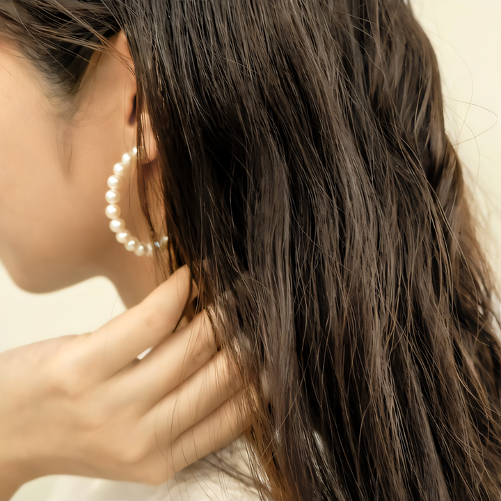 Close-up of a person wearing pearl hoop earrings with a blurred background