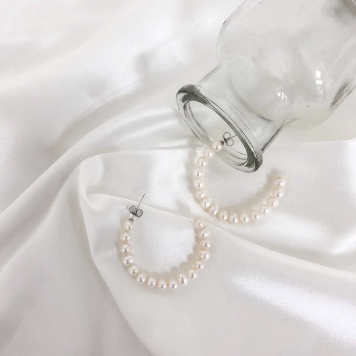 Pearl hoop earrings on a white fabric background with a glass jar.