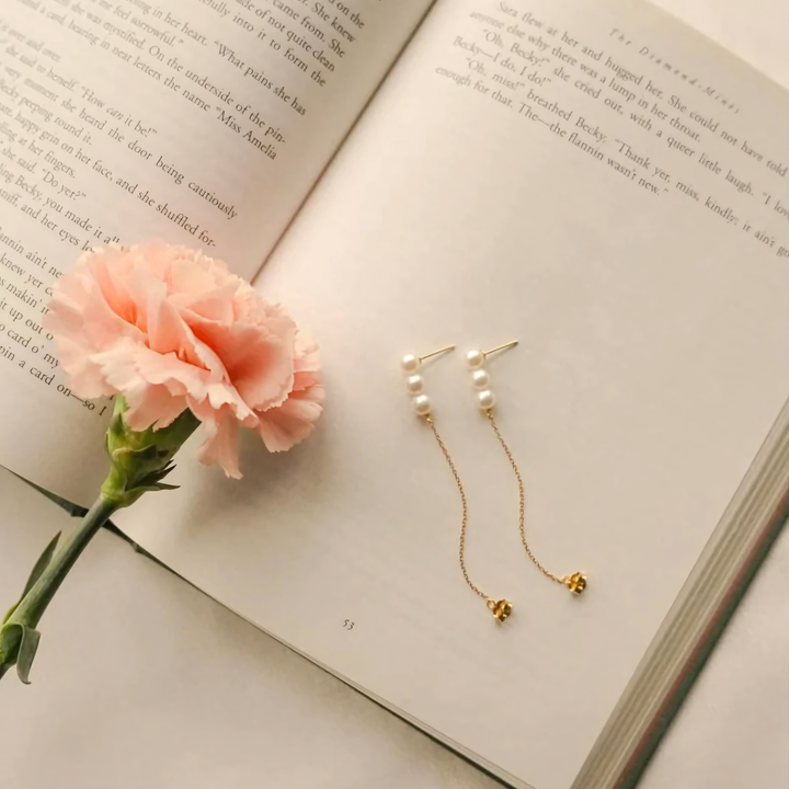 Pink carnation and pearl earrings on an open book