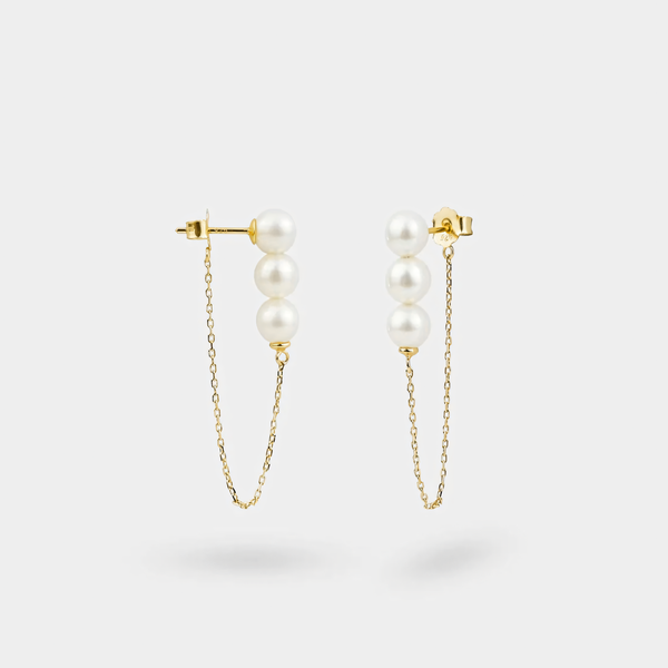 Pair of pearl earrings with gold chains on a light gray background