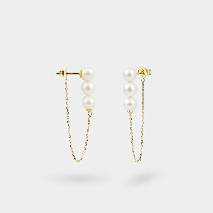 Pair of pearl earrings with gold chains on a light gray background
