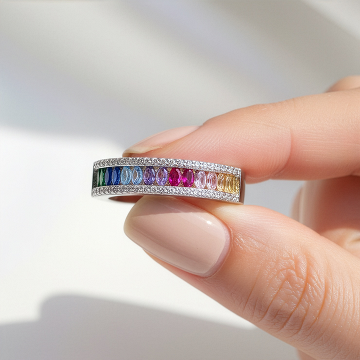 Ring with multicolored gemstones held by a hand on a light background
