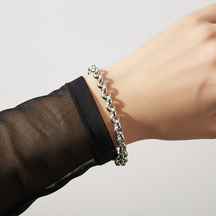Silver chain bracelet on a wrist with a plain background