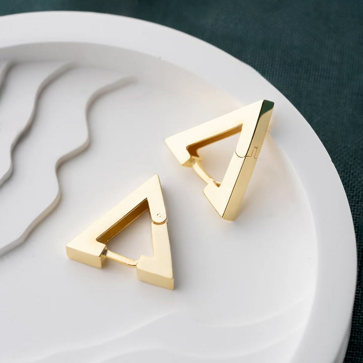 Gold triangle-shaped earrings on a white plate with a dark background