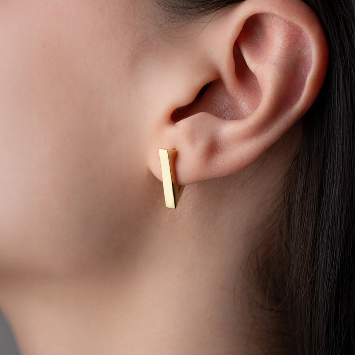 Gold bar earring worn by a person