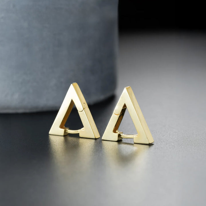 Gold triangle earrings on a reflective surface with a blurred background